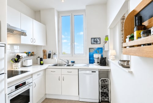 Cuisine blanche moderne avec étagères en bois, lave-vaisselle et baies vitrées vue mer aux Paris Normands, Boulogne