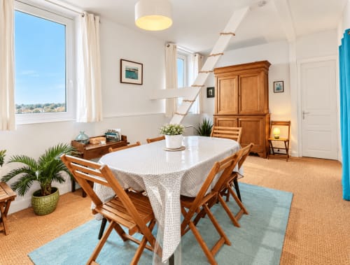 Salle à manger lumineuse avec mobilier en bois, vue sur mer depuis les fenêtres, plantes et équipements modernes aux Paris Normands