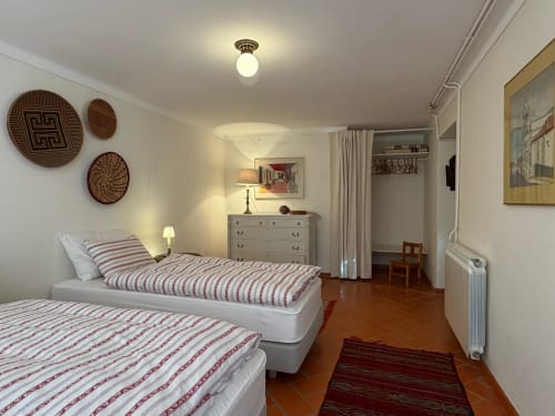 Quarto duplo com roupa de cama às riscas, cestos de palha na parede e vista para o jardim em Quinta da Mata de Baixo
