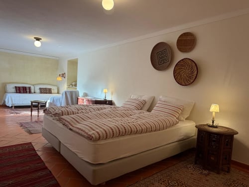 Quarto espaçoso na Quinta da Mata de Baixo com cama de casal, roupa de cama às riscas, cestos de vime na parede e vista para o jardim em Ferreira