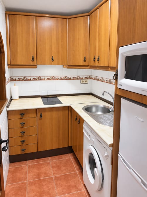 Cocina compacta en apartamento La Posada con muebles de madera, electrodomésticos blancos y piso de baldosa de barro en Oropesa