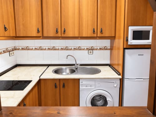 Cocina compacta del estudio La Posada, Oropesa Toledo, con muebles de madera, azulejos blancos, fregadero y lavadora