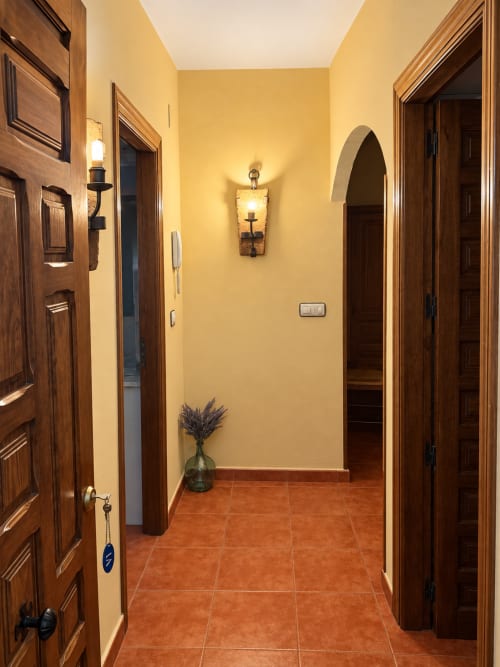 Pasillo de La Posada con puertas de madera, paredes amarillas, piso de barro y entrada de arco en Oropesa
