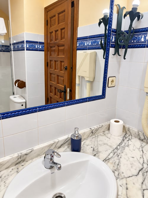 Elegante baño en La Posada Apartamentos, Oropesa Toledo, con encimera de mármol, azulejos blancos tipo metro y detalles azules decorativos