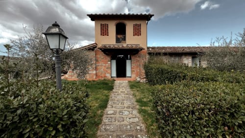 Ingresso del Borgo di Erboli a Cavriglia con edificio in terracotta, sentiero in pietra e siepi verdi