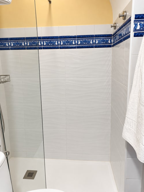 Moderno baño con azulejos blancos tipo metro, cenefa decorativa azul, ducha de lluvia y drenaje de granito en La