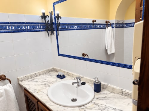 Lavabo de baño con encimera de mármol, espejo enmarcado en azul y azulejos blancos en apartamentos La Posada, Oropesa