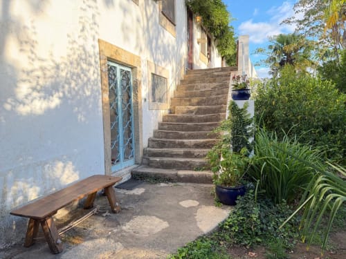 Escadaria de pedra com banco de madeira na Quinta da Mata de Baixo em Ferreira do Zêzere, cercada por jardim exuberante com vasos