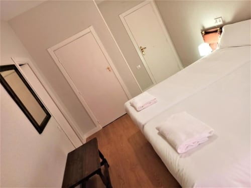 Habitación doble en Hotel del Trueno en Ezcaray con cama blanca, suelo de madera y varias puertas