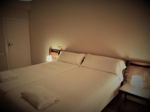Acogedora habitación doble del Hotel del Trueno en Ezcaray con iluminación cálida, cama de madera y ropa de cama color crema