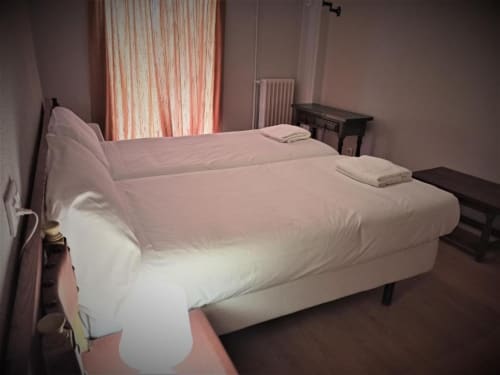Habitación doble en Hotel del Trueno en Ezcaray con camas gemelas, paredes rosa y ventana con persianas