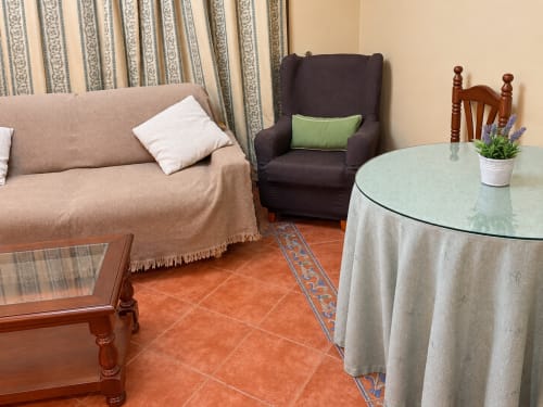 Acogedor salón de La Posada en Oropesa con sofá beige, sillón oscuro, mesa redonda y piso de barro