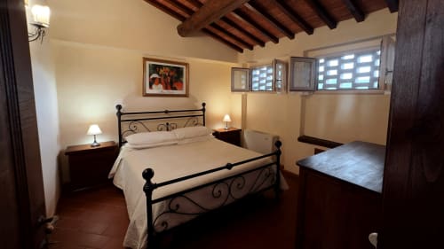 Camera da letto dell'appartamento Galileo a Borgo di Erboli, Cavriglia con letto in ferro battuto, travi in legno e arredi d'epoca