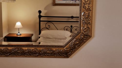 Specchio della camera che riflette il letto in ferro battuto con cuscini, lampada da comodino e tavolino presso Borgo di Erboli, Cavriglia
