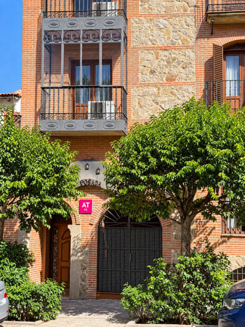 Entrada del hotel La Posada en Oropesa, Toledo con fachada de ladrillo, balcones ornamentales y puerta de patio cubierta de hiedra