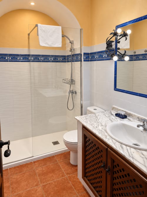 Baño moderno de La Posada Oropesa con ducha a ras de suelo, lavamanos de mármol, detalles en azulejos azules y toallero calefactado