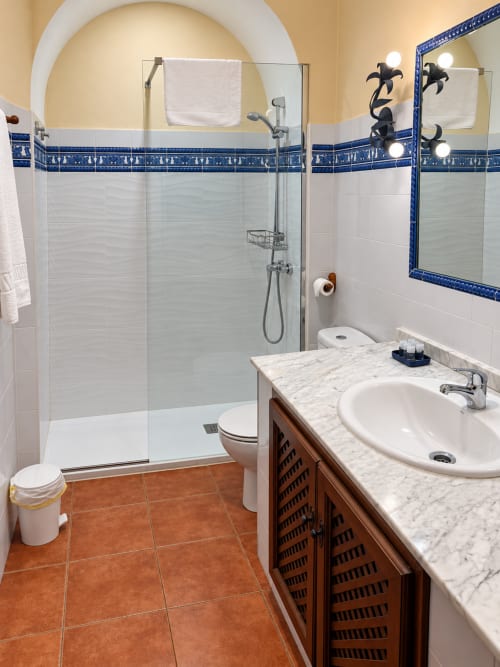 Baño de Apartamentos Turísticos La Posada en Oropesa con ducha de azulejos azules, lavamanos de mármol y piso de terracota