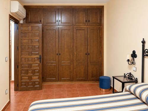 Dormitorio del apartamento La Posada en Oropesa con armario de madera, cama rayada y baldosas de terracota