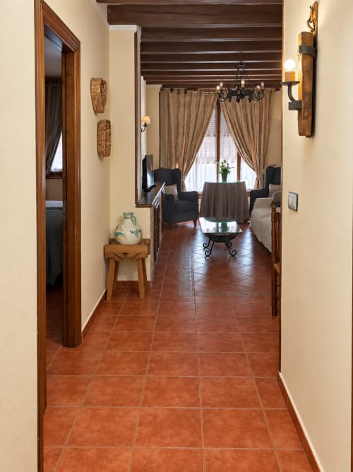 Pasillo del hotel apartamento La Posada en Oropesa, Toledo, con baldosas de terracota y techo de vigas de madera