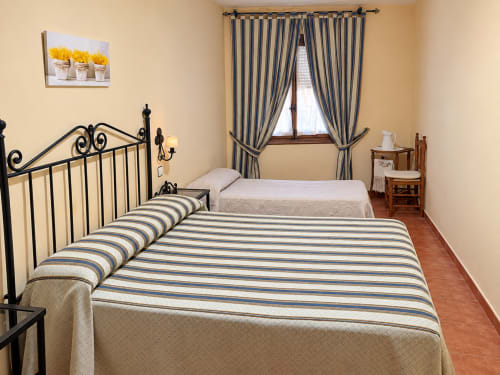 Habitación en La Posada Apartamentos, Oropesa Toledo con cama de sábanas rayadas, cabecero de metal y cortinas azules