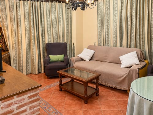 Sala de estar en el apartamento La Posada de Oropesa, Toledo, con sofá, sillón, mesa de madera y cortinas rayadas