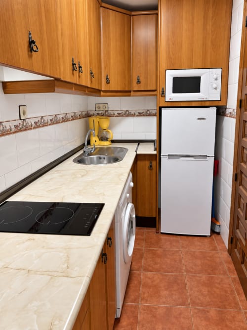 Cocina compacta en el apartamento La Posada, Oropesa, con gabinetes de madera, encimeras de mármol y electrodomésticos modernos