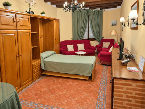 Estudio en La Posada, Oropesa Toledo, con cama, sofá rojo, muebles de madera y piso de barro cocido