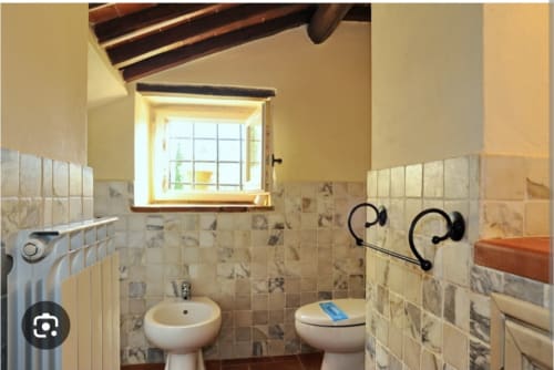 Rustic bathroom in Tommaso apartment at Borgo di Erboli, Cavriglia, featuring beige tiles, toilet, bidet, and wooden beams
