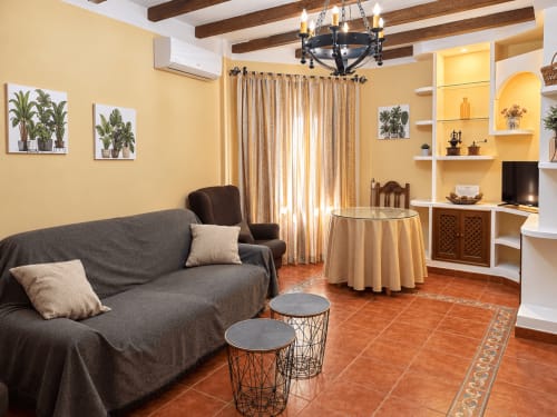 Apartamento La Posada en Oropesa, Toledo: sala acogedora con sofá gris, paredes amarillas, vigas de madera y pisos de terracota