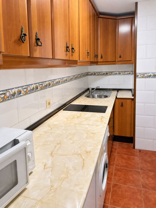 Cocina moderna con muebles de madera, encimera de mármol y azulejos blancos en Apartamentos La Posada, Oropesa, Toledo
