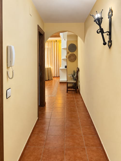 Pasillo estrecho con suelo de baldosa terracota, paredes color crema y puertas de madera oscura en Apartamentos Turísticos La Posada
