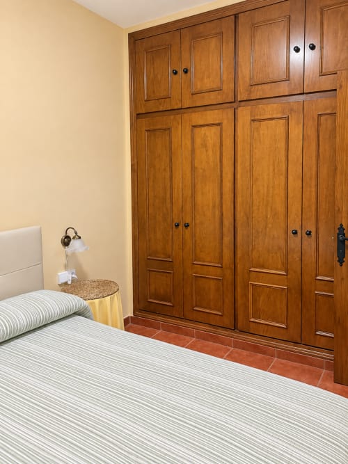 Dormitorio con cama a rayas, armario de madera y mesita de noche de mimbre en La Posada, Oropesa