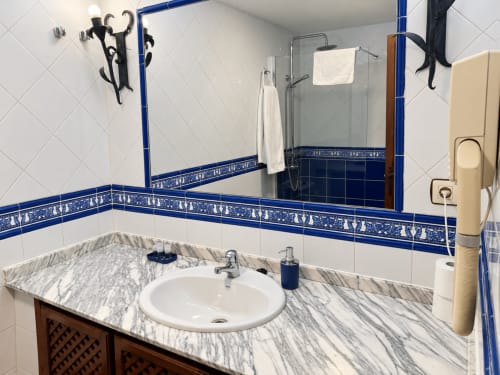 Baño en La Posada Apartamentos Turísticos de Oropesa, Toledo, con encimera de mármol, azulejo con cenefa azul y cristal