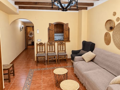 Acogedor salón de La Posada, Oropesa con paredes beige, vigas de madera, piso de barro, sofá y comedor