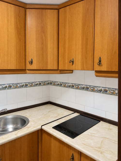 Rincón de cocina en apartamento La Posada, Oropesa con muebles de madera, encimera de mármol, placa de inducción y azulejos blancos