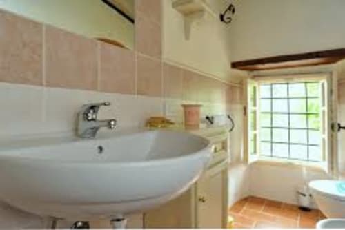 Bagno luminoso nell'appartamento Lapo a Borgo di Erboli, Cavriglia, con lavabo curvo, pareti piastrellate e porta in vetro verso il giardino