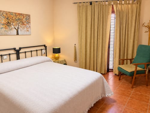 Habitación luminosa del hotel La Posada en Oropesa con cama queen, silla verde y pisos de terracota