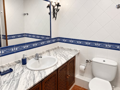 Baño moderno del hotel La Posada en Oropesa con tocador de mármol, lavabo redondo, azulejos azules y inodoro