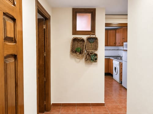 Pasillo de apartamento La Posada con puertas de madera, baldosas de barro y cestas tejidas decorativas en Oropesa, Toledo