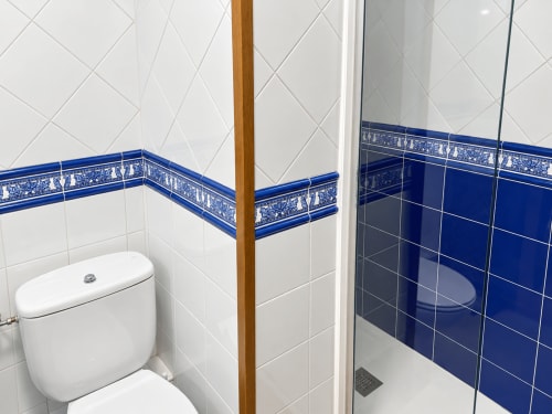 Baño moderno del apartamento La Posada, Oropesa Toledo, con azulejos blancos, cenefa azul decorativa, inodoro y ducha