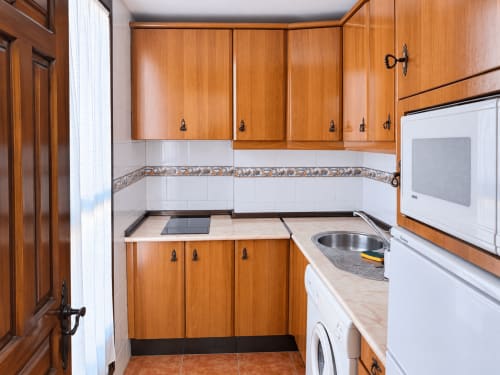 Cocina compacta con muebles de madera, electrodomésticos blancos y azulejos en la pared de Apartamentos La Posada en Oropesa
