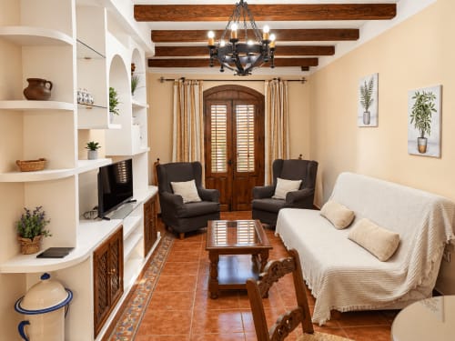 Amplio salón en La Posada hotel de Oropesa con paredes crema, vigas de madera, sillones oscuros y sofá