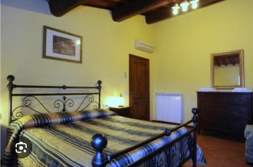 Camera da letto dell'appartamento Eleonora al Borgo di Erboli di Cavriglia con letto in ferro battuto, pareti gialle e arredi d'epoca