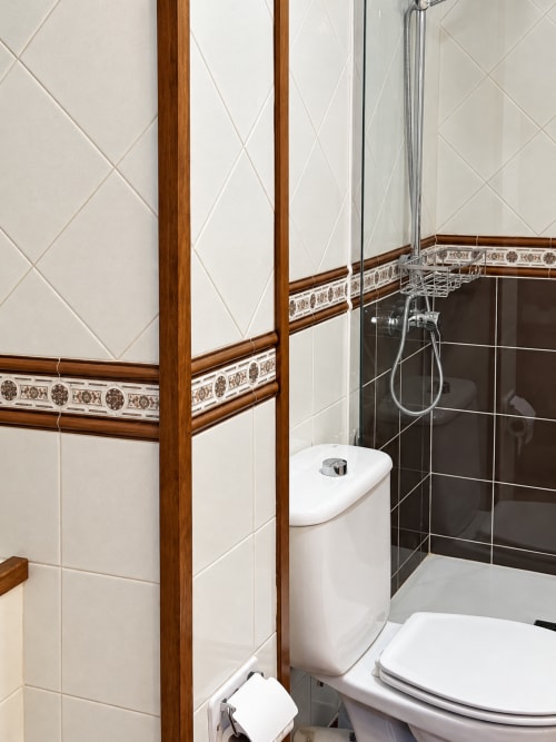 Baño moderno en La Posada Apartamentos, Oropesa, Toledo con azulejos blancos, ducha oscura y detalles de madera