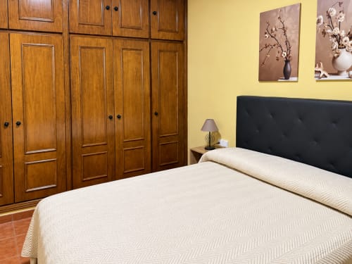 Habitación en apartamentos La Posada de Oropesa, Toledo con ropa de cama color crema, cabecero negro, armario de madera y paredes amarillas