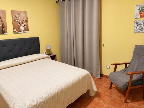 Habitación amarillo brillante en La Posada de Oropesa, Toledo con cama de cabecera negra, ropa de cama beige y silla de madera