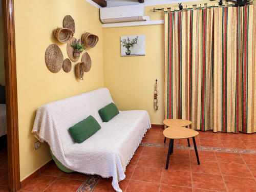 Luminosa sala de estar amarilla en La Posada, Oropesa con sofá blanco, cestería tejida y cortinas a rayas