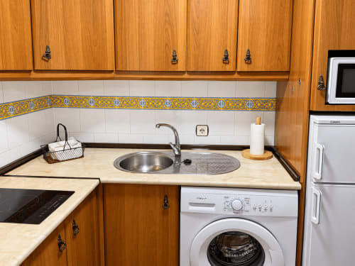 Cocina del apartamento La Posada en Oropesa con muebles de madera, azulejos decorativos y lavadora