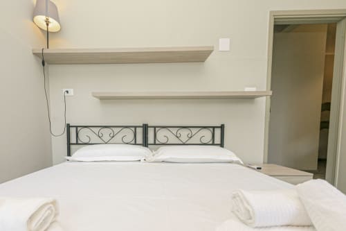 Camera moderna presso l'appartamento ML White House a Genova con letto in ferro battuto, lenzuola bianche, scaffali in legno e lampada a sospensione