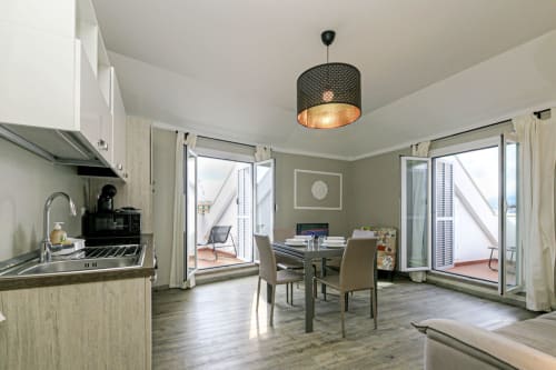 Cucina e zona pranzo in moderno appartamento a Genova con luci a sospensione, accesso alla terrazza e arredi contemporanei
